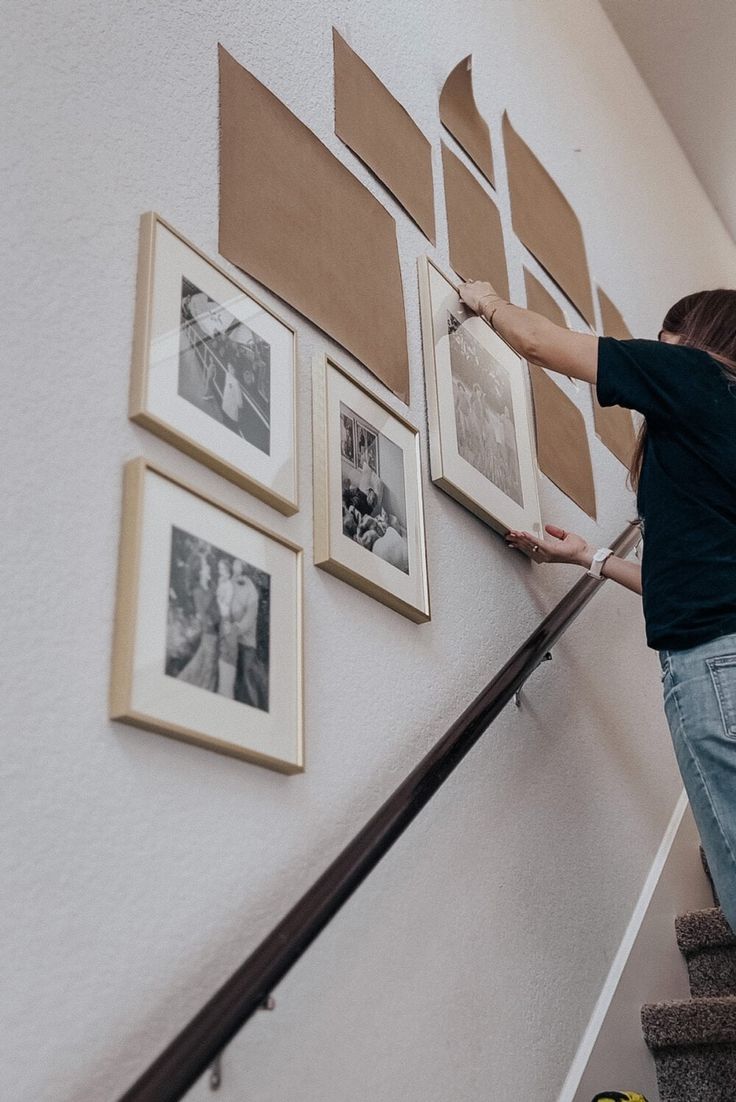 a woman is climbing up the stairs with her hand on the railing and pictures hanging on the wall