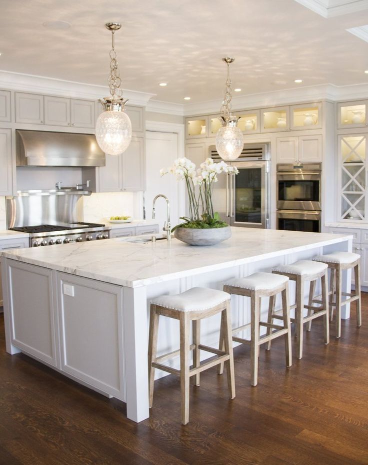 a large kitchen with white cabinets and marble counter tops, an island with four stools