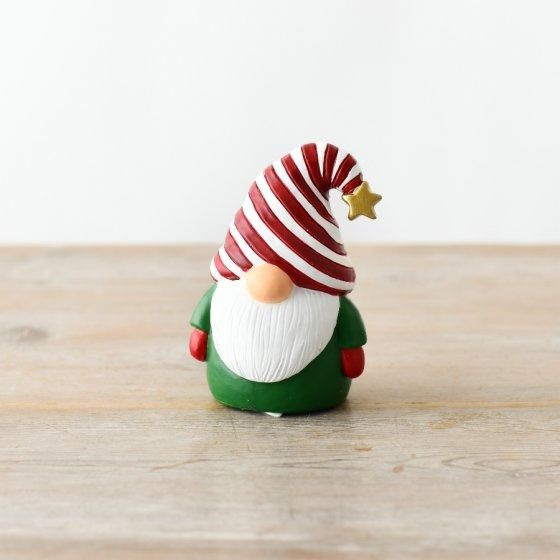 a small green and red santa clause figurine on a wooden table with a white wall in the background