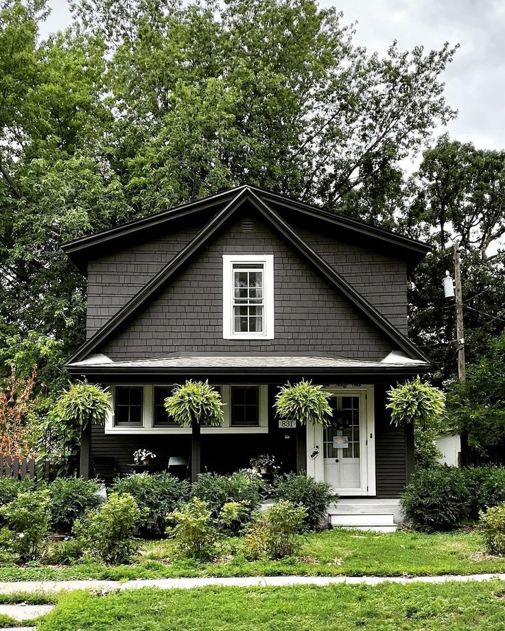 a black and white house surrounded by greenery in front of trees, grass and bushes