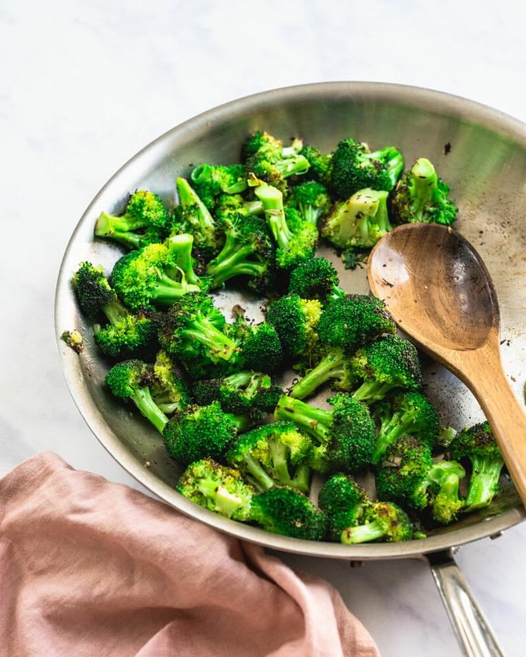 broccoli is being cooked in a pan with a wooden spoon on the side