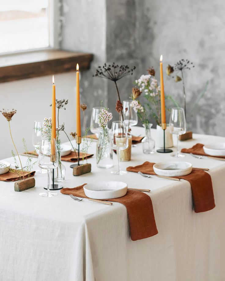 the table is set with white plates and brown napkins, candles, and flowers