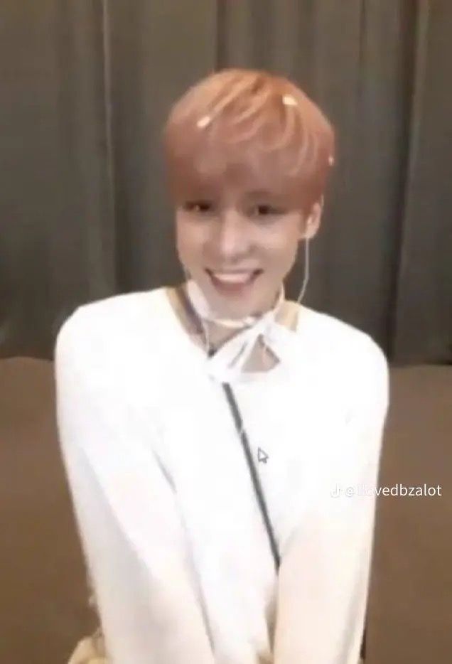 a young man with red hair and piercings standing in front of a wall wearing a white shirt