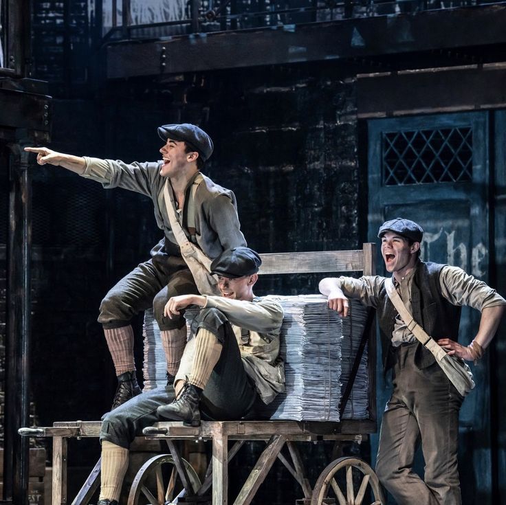 two men in period clothing on stage with one pointing at another man sitting on a cart