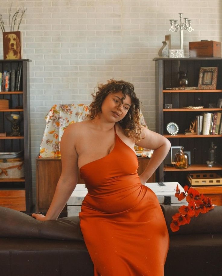 a woman in an orange dress leaning on a couch