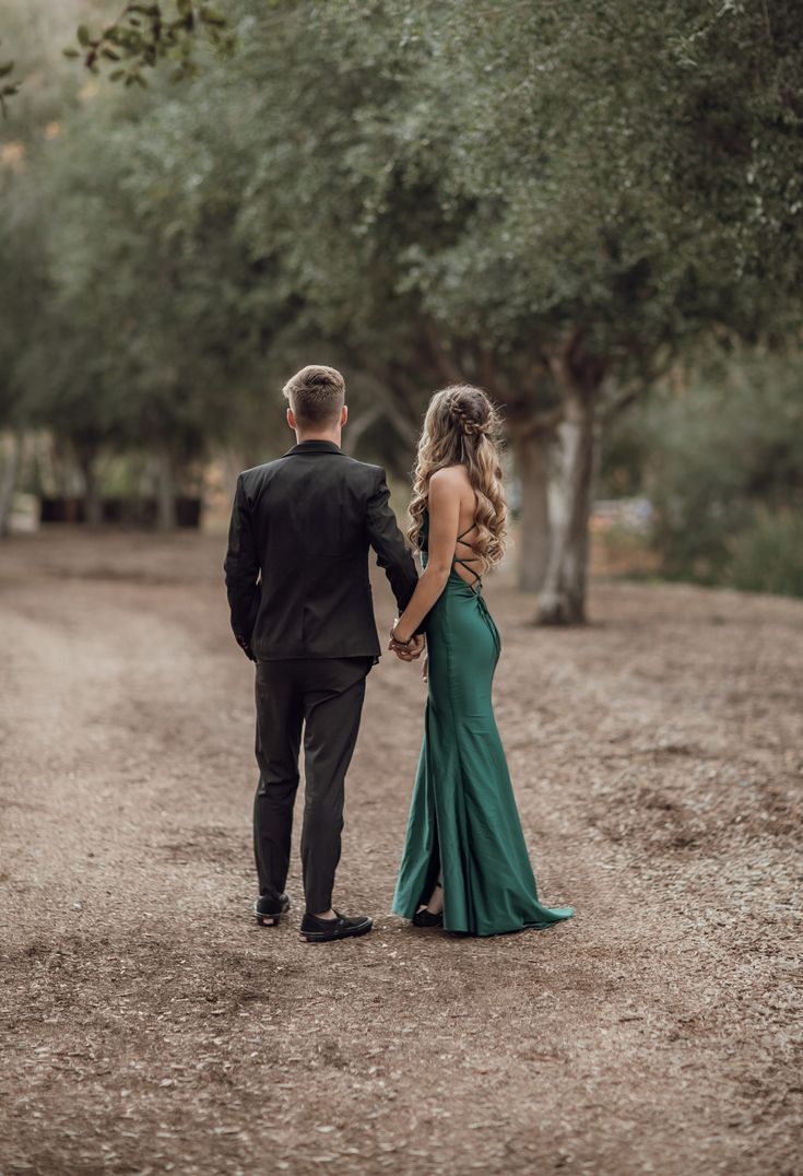 a man and woman walking down a dirt road holding hands