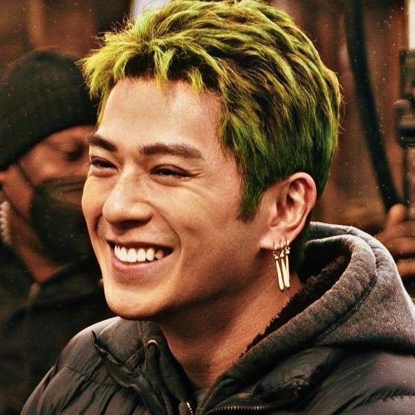 a young man with green hair and piercings on his ears smiles at the camera