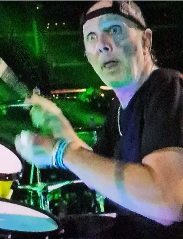 a man is playing drums on stage with green lights in the backgroung