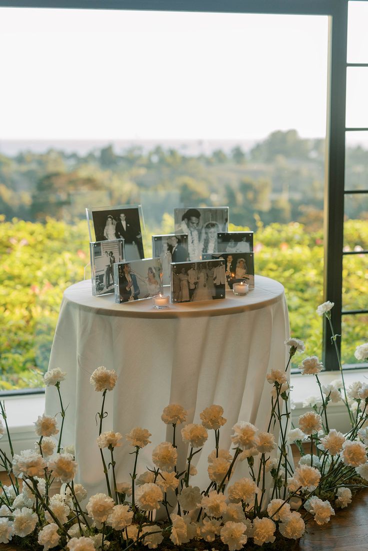 a table with flowers and pictures on it in front of a window overlooking the trees