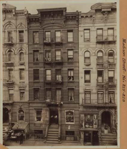 an old black and white photo of buildings in new york city with people standing on the steps