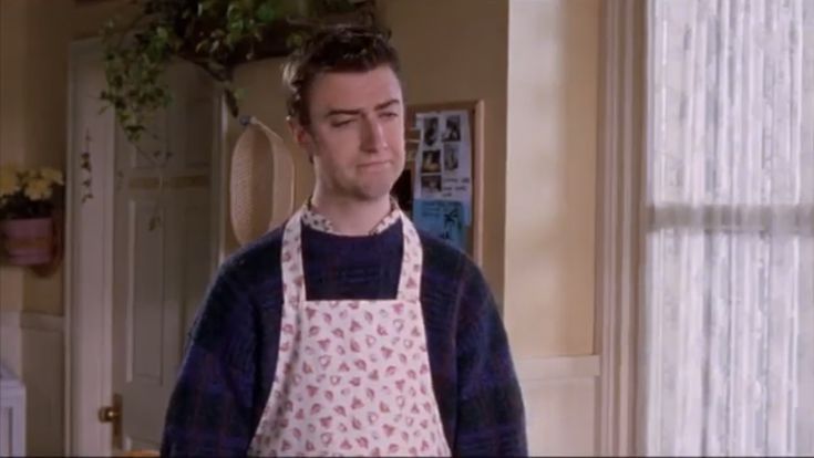 a man wearing an apron standing in front of a kitchen door with the curtains open