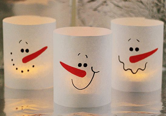 three frosty cups with faces drawn on them and lit candles in the shape of snowmen