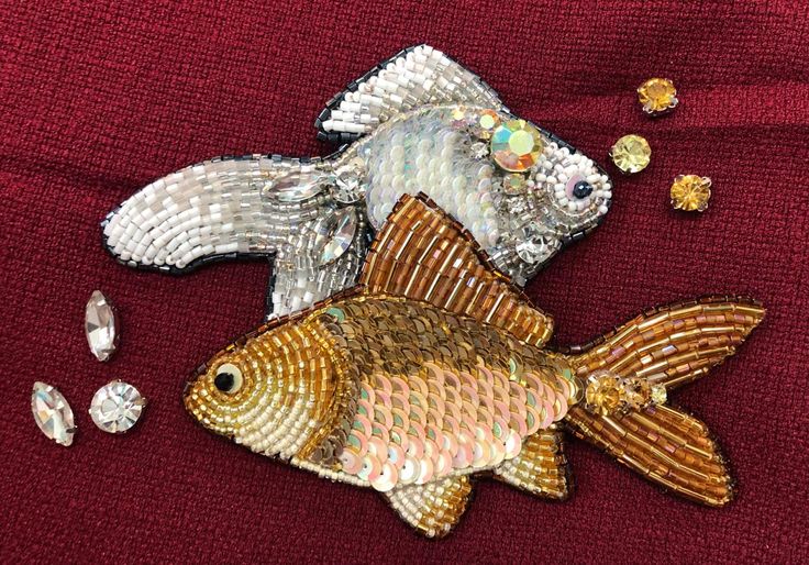 two gold and silver fish on a red cloth with some jewels around them, one is laying down