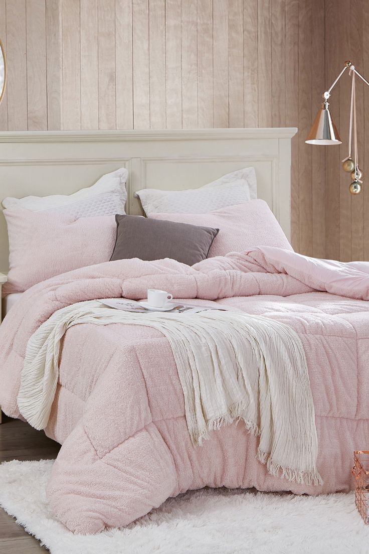 a bed with pink comforter and pillows in a bedroom