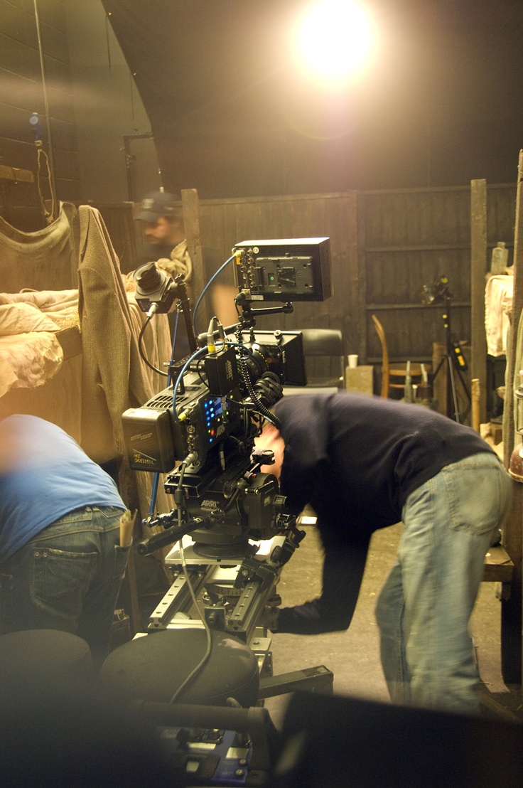 two men are working on a camera in a room full of wood and other items