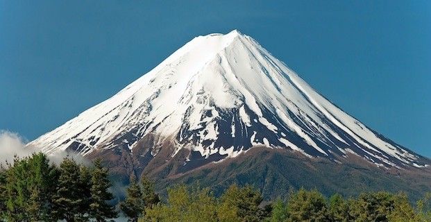 a snow covered mountain with trees in the foreground and a blue sky above it