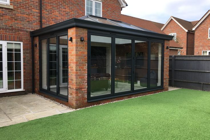 a brick building with glass walls and sliding doors on the outside, next to a green lawn