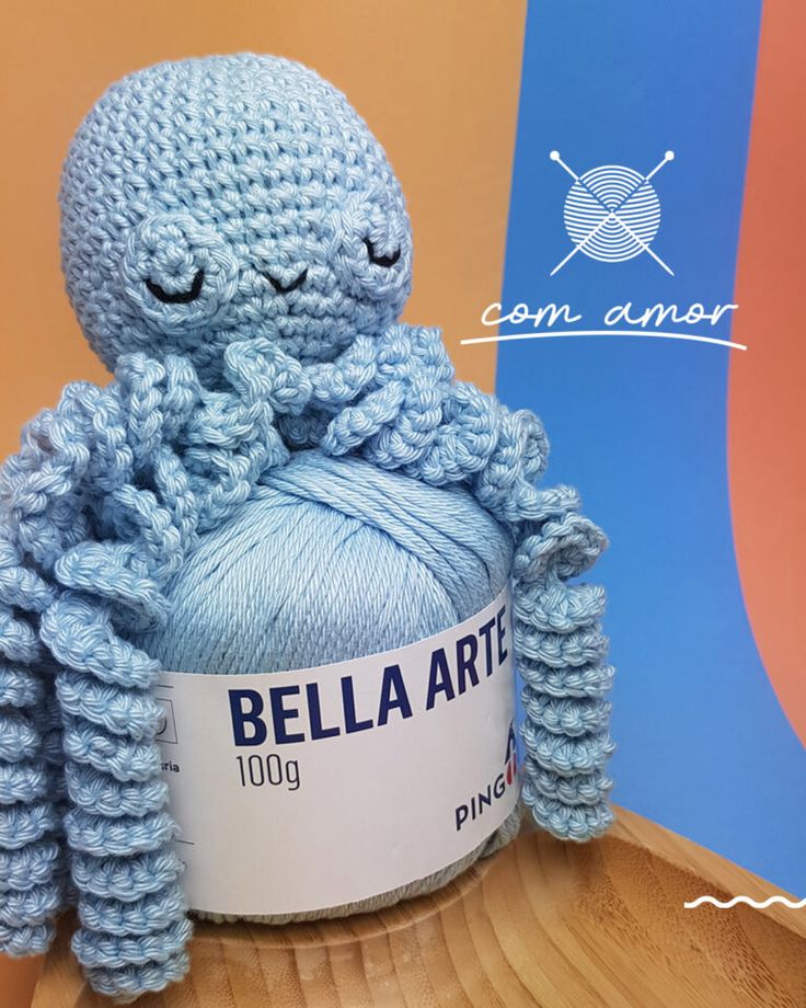 a blue crocheted octopus sitting on top of a ball of yarn with its eyes closed