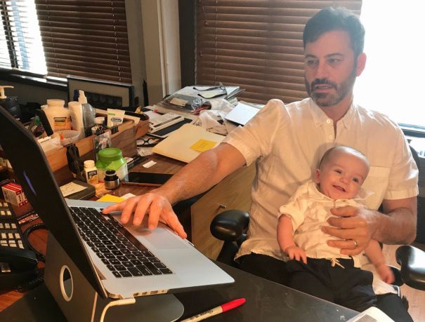 a man sitting in front of a laptop computer holding a baby