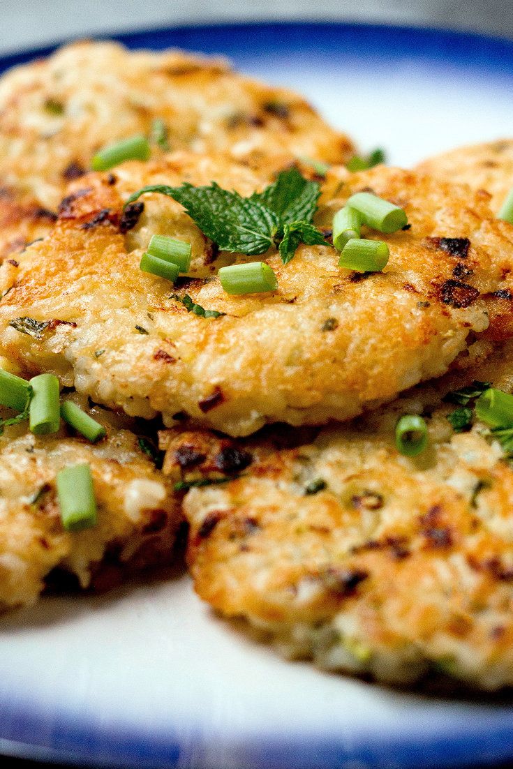 three crab cakes on a blue and white plate with green garnishes, ready to be eaten