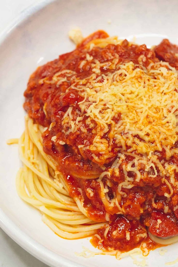 a white plate topped with spaghetti covered in sauce and parmesan cheese on top