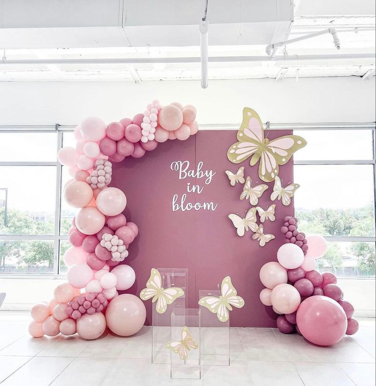 a pink and gold baby shower backdrop with balloons in the shape of butterfly's