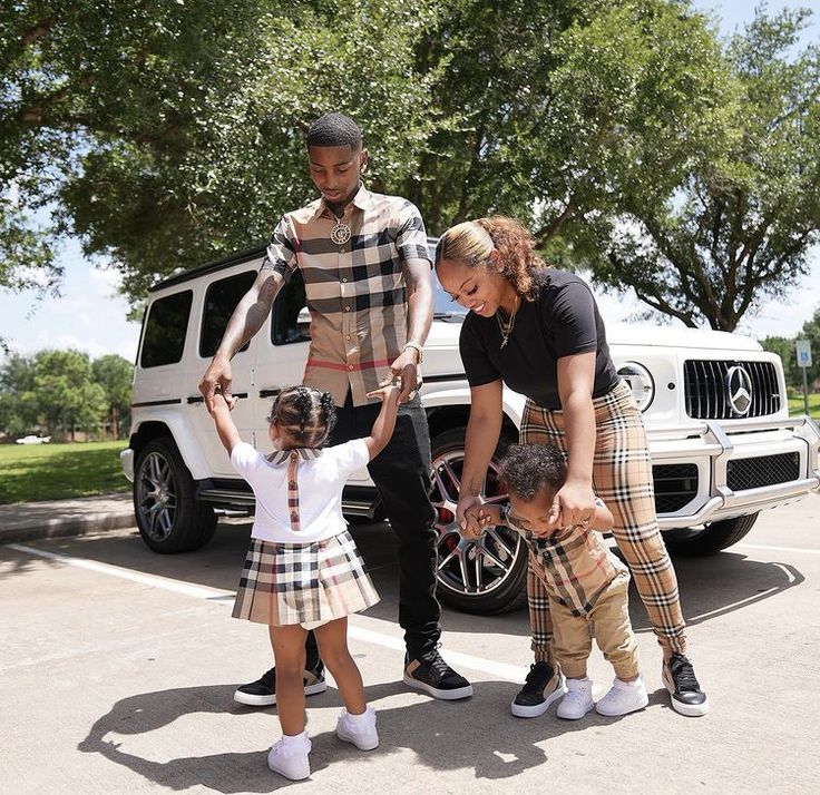 a man, woman and two children are standing in front of a white suv with their hands on the wheel