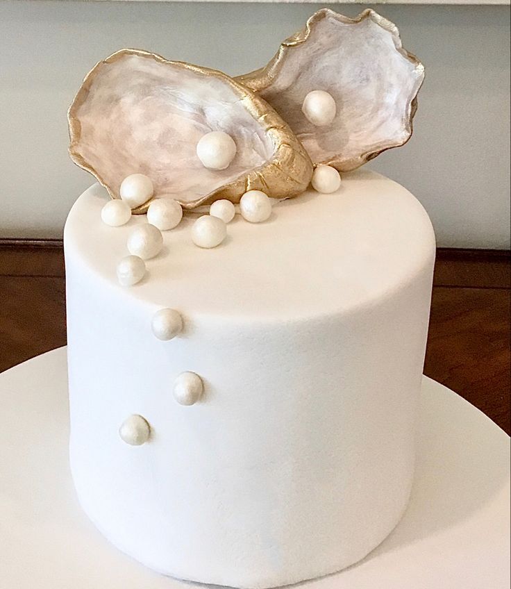 a close up of a white cake with pearls on the top and two large seashells