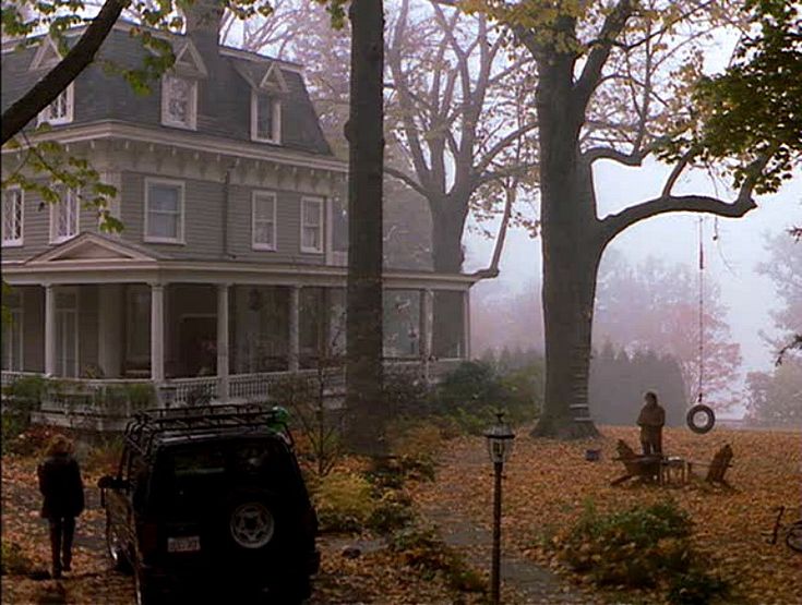 two people are standing in front of a house on a foggy day with their cars parked