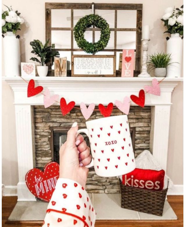 someone is holding two coffee mugs in front of a fireplace with hearts on it