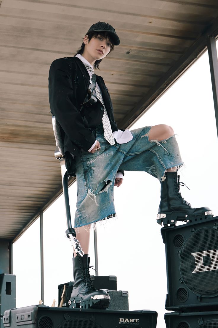 a man sitting on top of two speakers in front of a building and wearing a hat