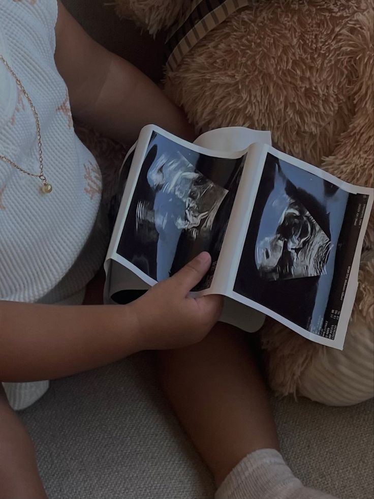 a person sitting on the floor reading a book with a teddy bear in the background