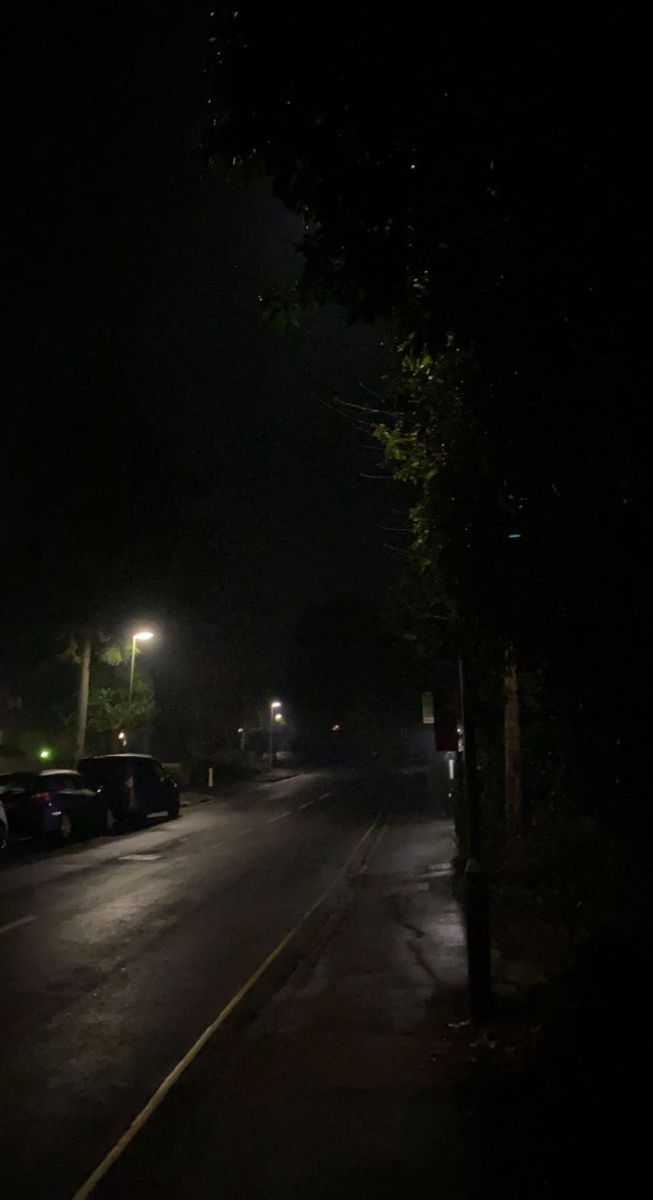 cars parked on the side of an empty street at night with no one in it