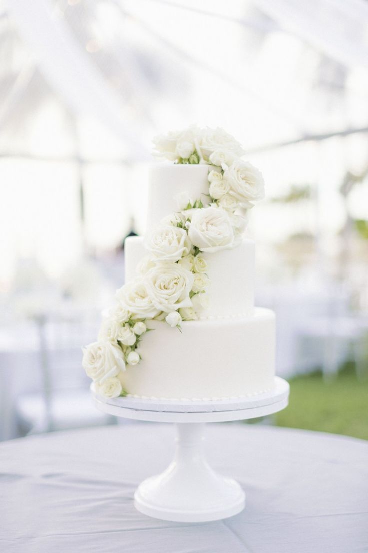 a wedding cake with white flowers on top sits on a table in front of a tent