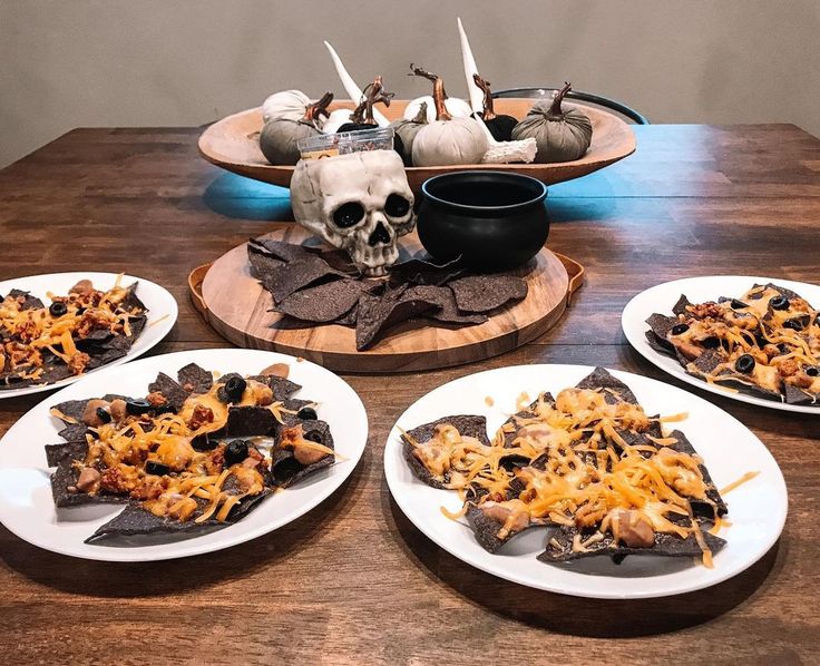 plates with nachos on them and a skull in the middle, sitting on a wooden table