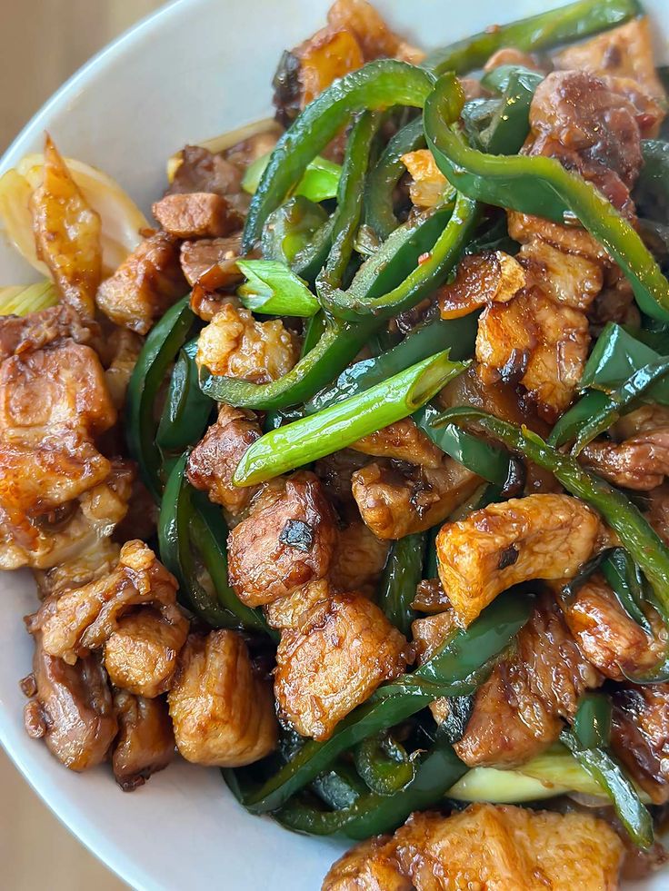 a white bowl filled with meat and green peppers on top of a wooden table next to an orange slice