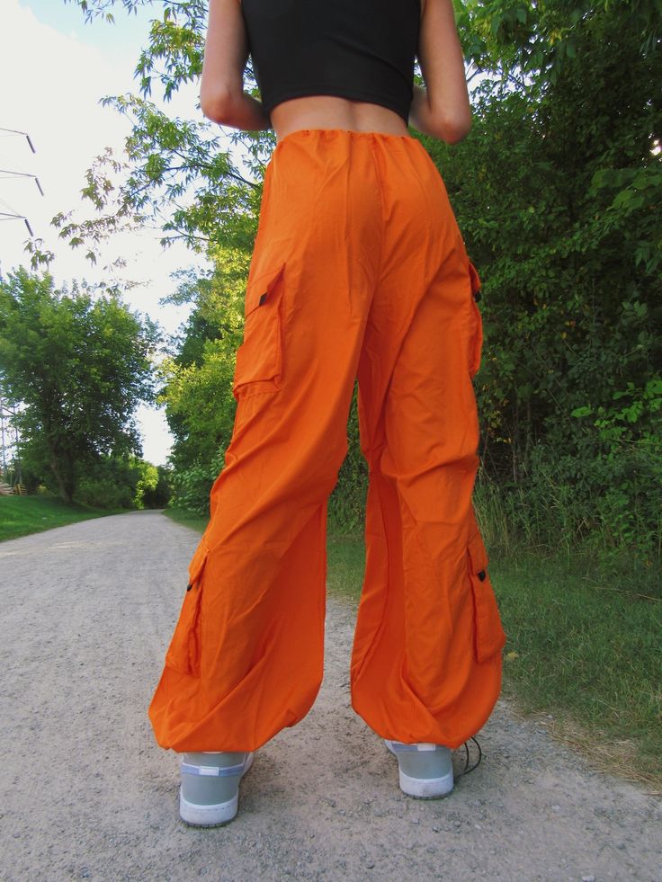 These bright orange cargo/parachute pants are the coolest Fall and Winter wardrobe staple. Featuring 4 pockets, an adjustable drawstring cord waistline, and adjustable cord drawstring ankles. Emily is wearing size S. Summer Utility Parachute Pants For Outdoor Activities, Nylon Cargo Pants For Summer Hiking, Summer Nylon Cargo Pants For Hiking, Utility Parachute Pants With Drawstring For Outdoor Activities, Spring Cargo Pants With Drawstring For Outdoor Activities, Nylon Parachute Pants With Drawstring For Outdoor, Nylon Parachute Pants With Drawstring For Outdoor Activities, Summer Hip Hop Cargo Style Parachute Pants, Spring Hiking Cargo Pants With Side Pockets