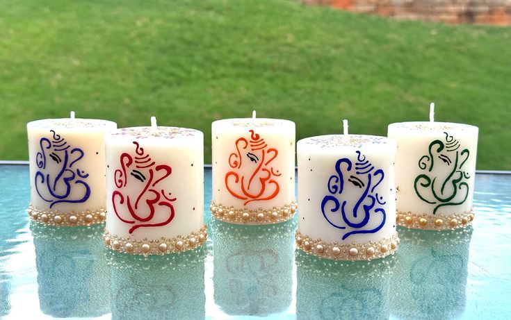 four candles with designs on them sitting in front of a pool