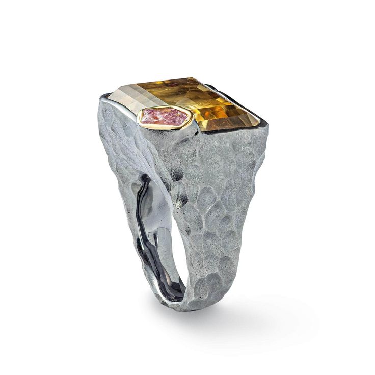 A bold and generous ring featuring a prominent emerald-cut Citrine as its centerpiece, paired with a raw Pink Sapphire on the side for an unexpected twist. The textured Silver band, plated with Black Rhodium and accented with 18K Gold, adds depth and contrast to the design. This one-of-a-kind piece embodies artistic self-expression, crafted for someone who embraces a bold style. A unique creation with no duplicates, meant for a wearer who values originality and makes a statement. Metal: 925 Silver Stones: Citrine, Rough Sapphire Plating: Black Rhodium, 18K Gold  PLEASE NOTE: This design showcases a natural raw gemstone that may exhibit raw edges, inclusions, cracks, and color banding. These are not flaws but marks of gem authenticity. Natural gemstones may appear different under various li Fine Art Jewelry, Gold Gifts, Bold Style, Lemon Quartz, Black Rhodium, Green Amethyst, Raw Gemstones, Red Garnet, Showcase Design