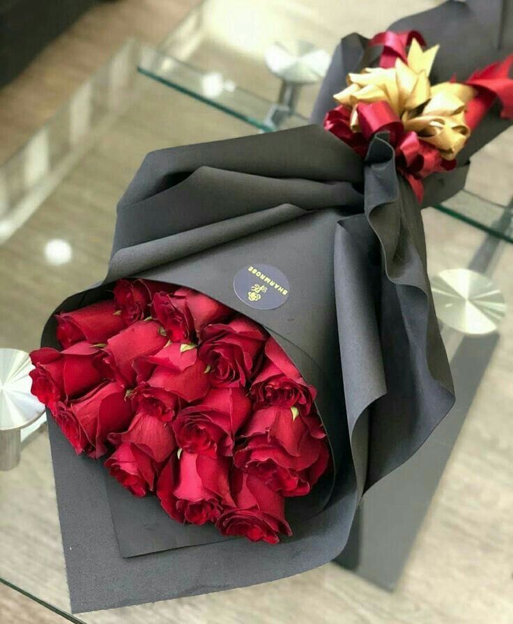 a bouquet of red roses wrapped in black paper and tied to a gray box on a glass table