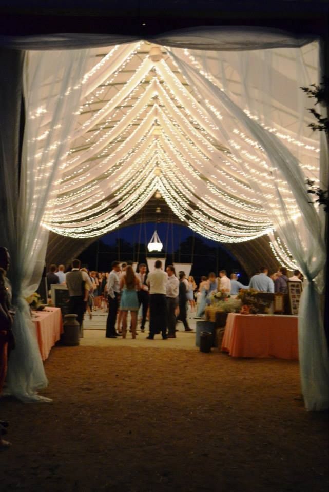 a group of people that are standing under a white tent with lights on it's sides