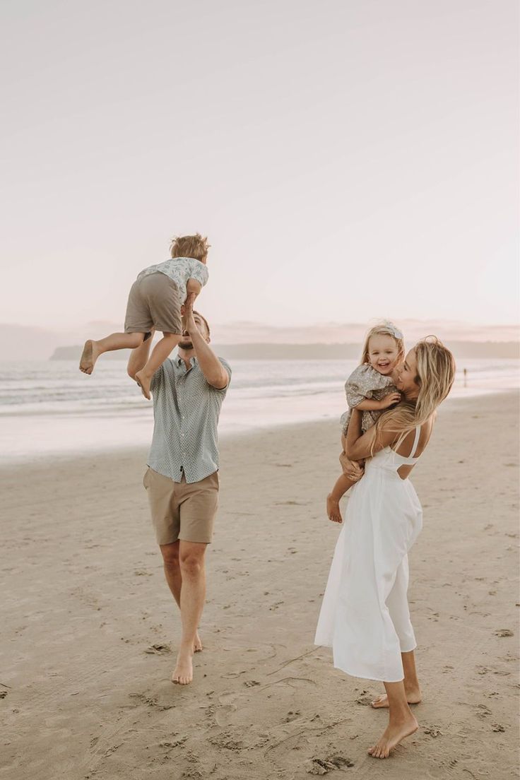 a man and woman walking on the beach with a baby in their arms while holding an infant