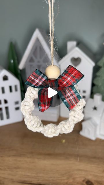 a christmas ornament hanging from a rope with a bow on the top and a house in the background