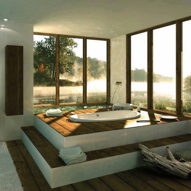 a bath tub sitting on top of a wooden floor next to large windows and trees