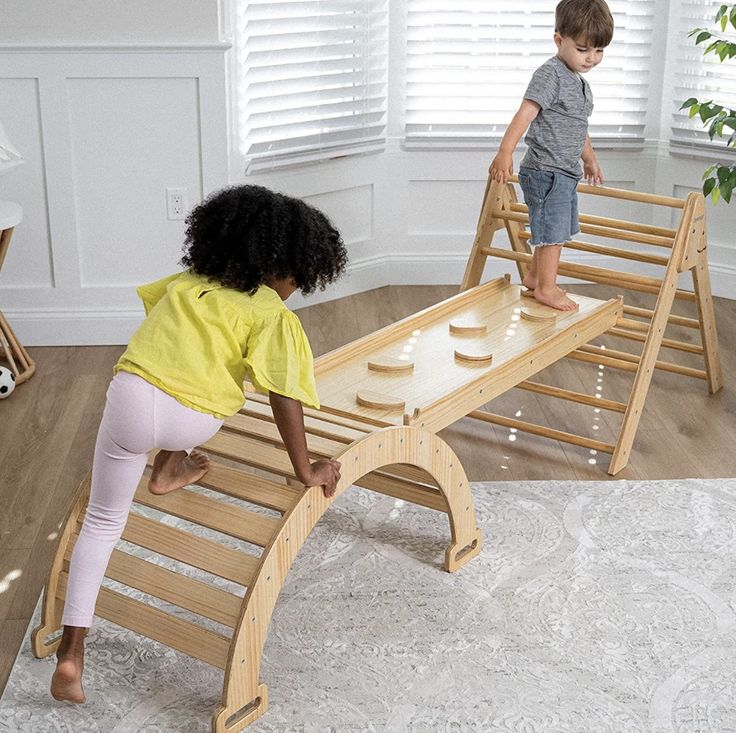 two children playing on a wooden bench in a room with white walls and hardwood floors