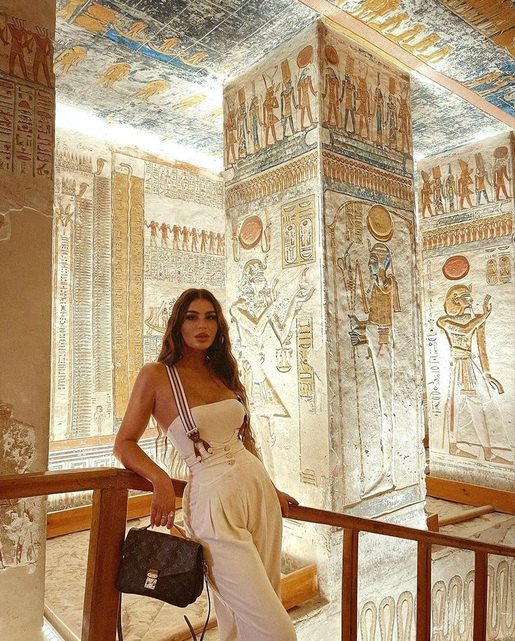 a beautiful woman standing in front of some egyptian wall paintings on the side of a building