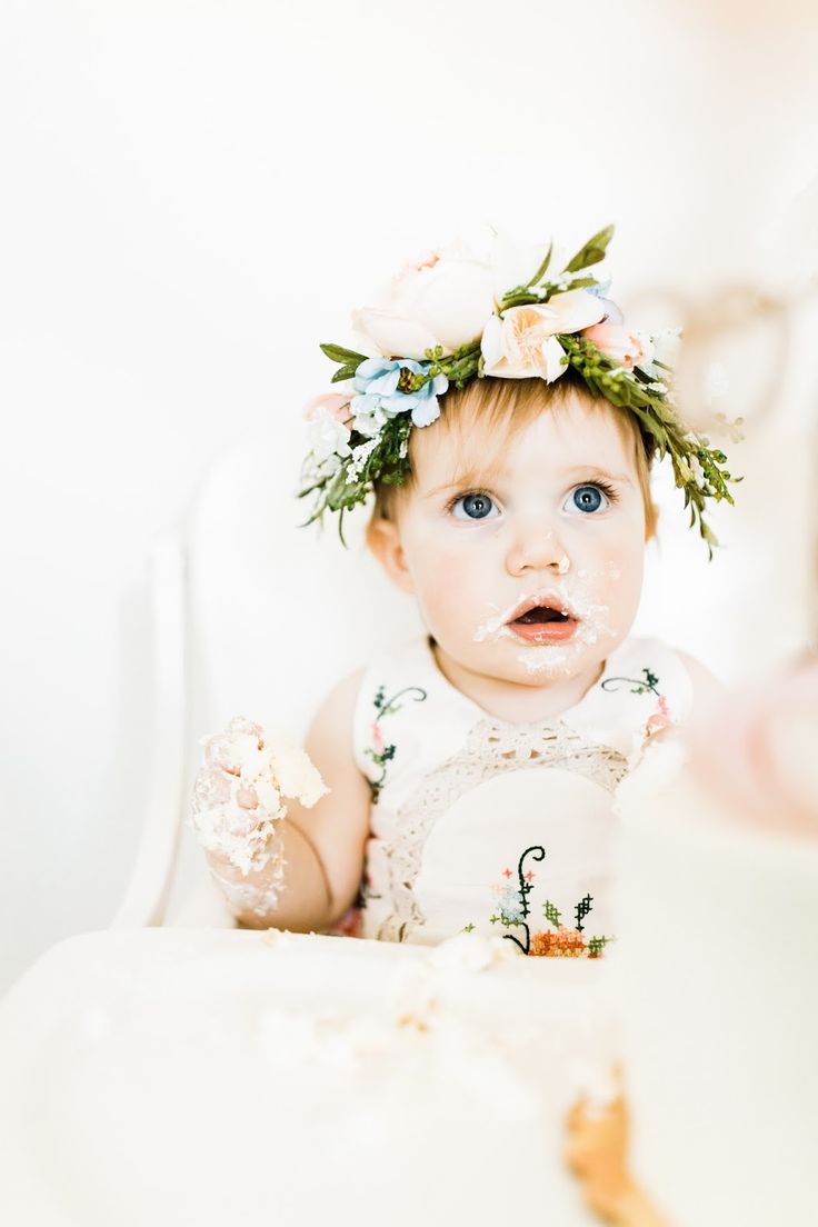 a baby girl with cake on her face and flowers in her hair is looking at the camera