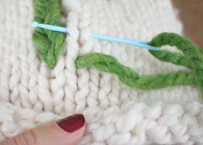 someone is stitching together yarn on a white knitted blanket with blue pins in the middle