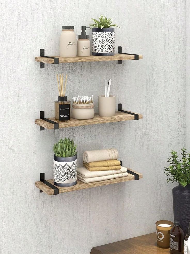 three wooden shelves with plants, candles and other items on them against a white wall