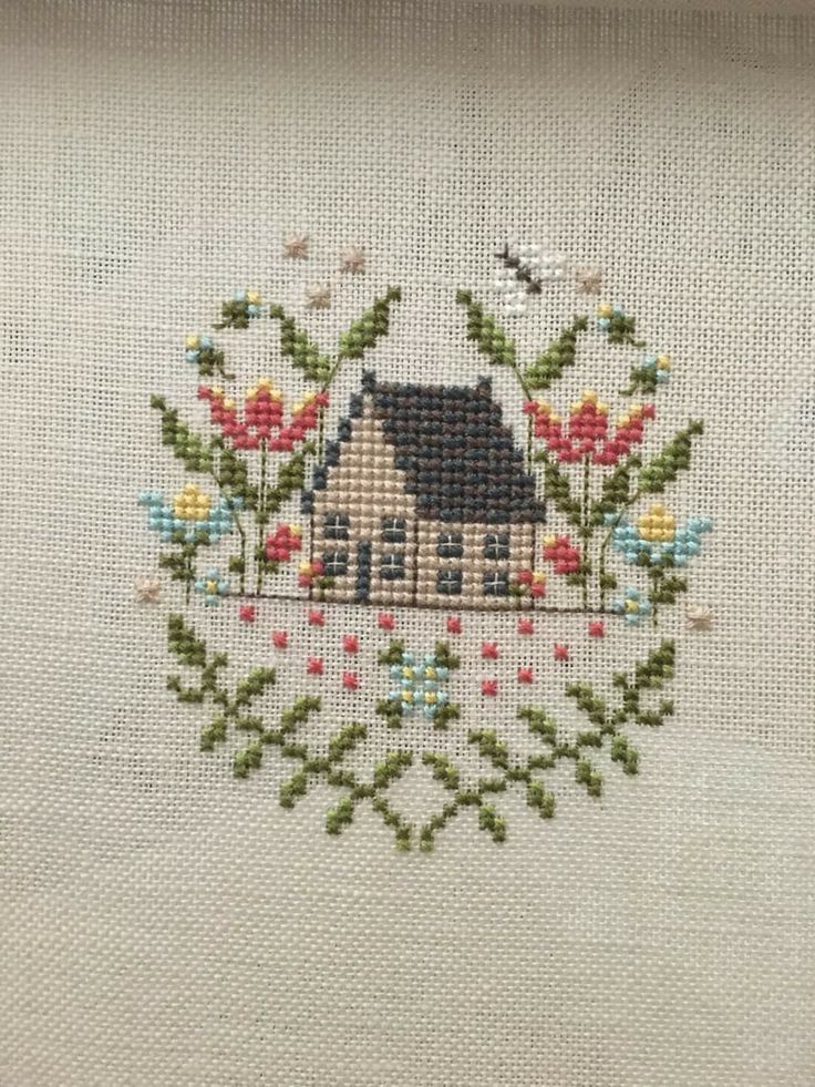 a cross stitch house with flowers and birds in the center on a white cloth background